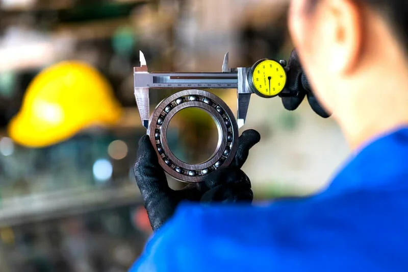 A person using calipers to measure the diameter of a bearing.