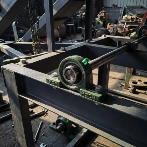 Pillow block bearing installed on a dusty conveyor system in a factory.